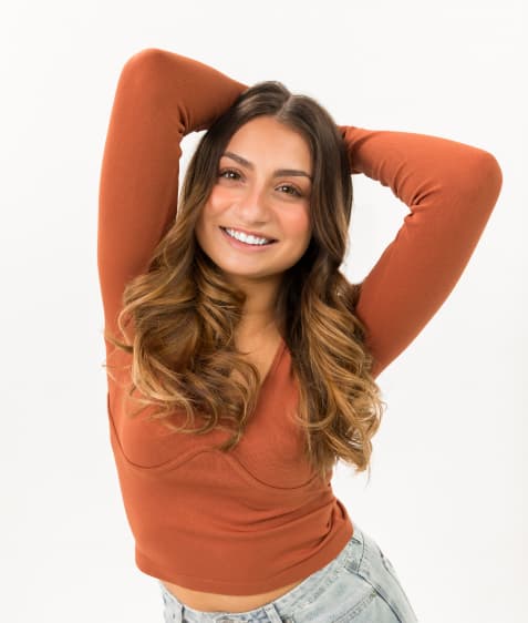 Woman with long sleeved shirt and balayage hair smiles at camera.