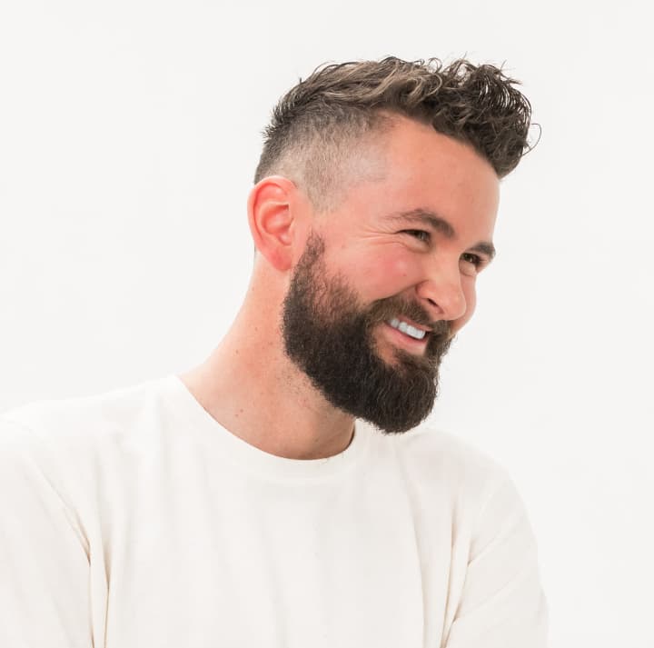 Man with fade haircut and groomed beard, smiling to the right.